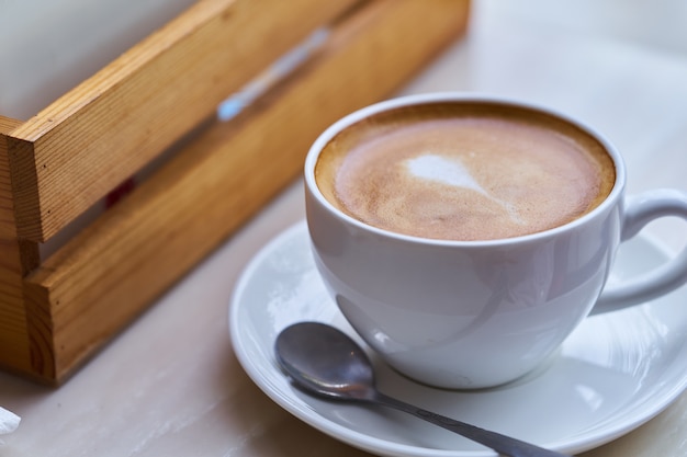 Een kopje koffie in een witte kop op tafel, hete latte koffie in café.