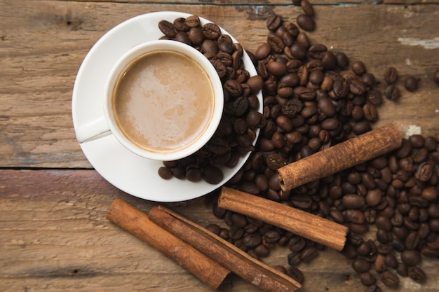 Een kopje koffie, koffiezaden, kaneel en een boek op een houten tafel