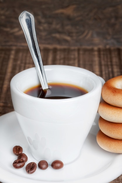 Een kopje koffie met een lepel en gedroogde bagels. Op een houten tafel textuur.