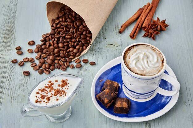 Een kopje koffie met slagroom en melk, gehakte chocolade en een zak koffiebonen op een blauwe houten tafel. Weense koffie
