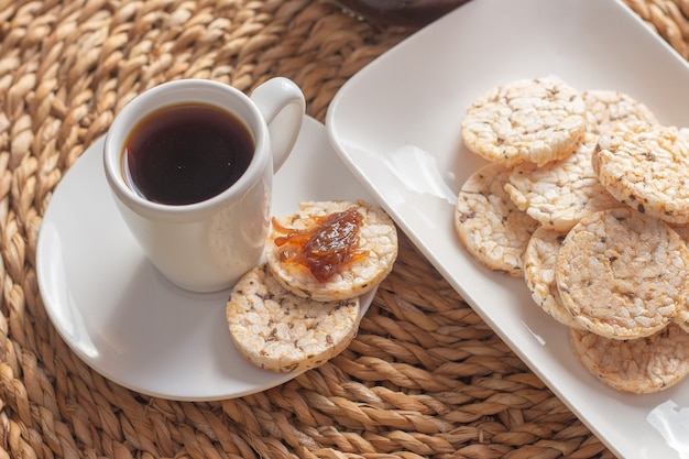 Een kopje koffie onder de strotafel omringd door een kom vol rijstkoekjes en een jelly pot