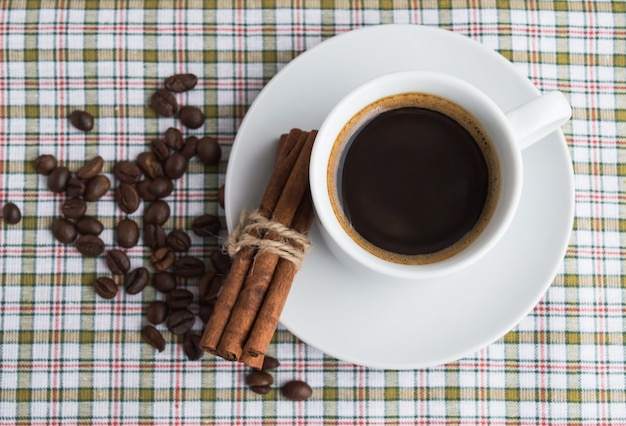 Een kopje koffie op lichte achtergrond met kaneel en koffiebonen. Bovenaanzicht