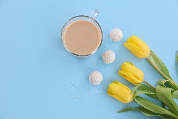 Een kopje koffie snoep en gele tulpen op een blauwe achtergrond