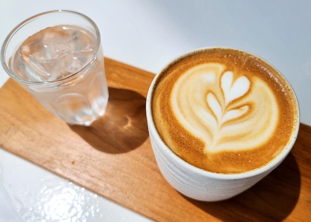 Een kopje latte art koffie met drinkwater op een houten bord