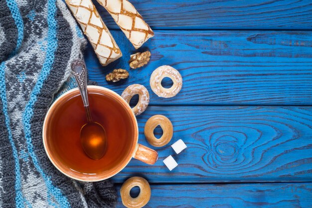 Een kopje thee, een gebreide sjaal en bagels op de achtergrond van blauwe houten tafel