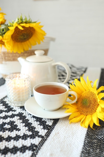 Een kopje thee en een theepot met een kaars op een tafel met zonnebloemen, theetijdesthetiek