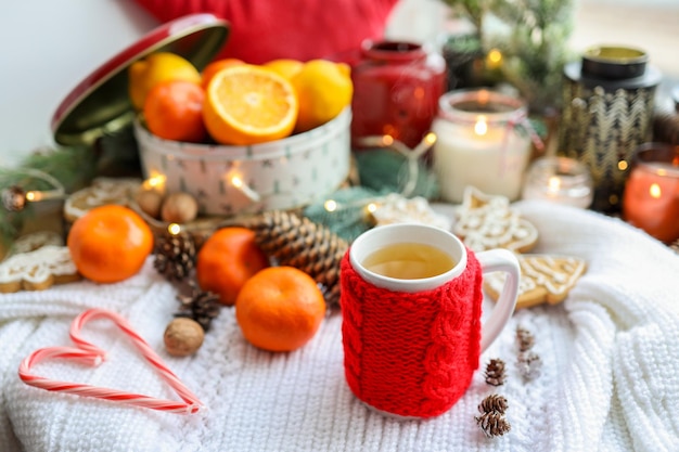 Een kopje thee met een gebreide rode decoratie mandarijnen kaarsjes een guirlande Kerstsfeer in huis