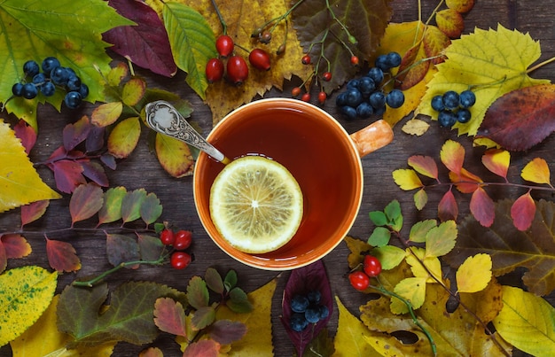 Foto een kopje thee op een achtergrond van veelkleurige herfstbladeren en druiven op een houten ondergrond