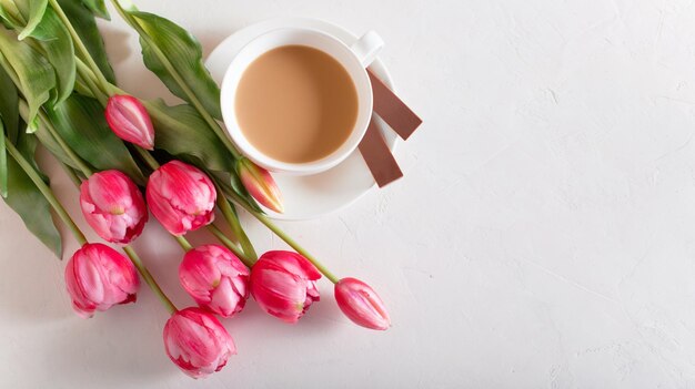 Een kopje warme ochtendkoffie melkchocolade en een boeket roze-lila tulpen op witte achtergrond