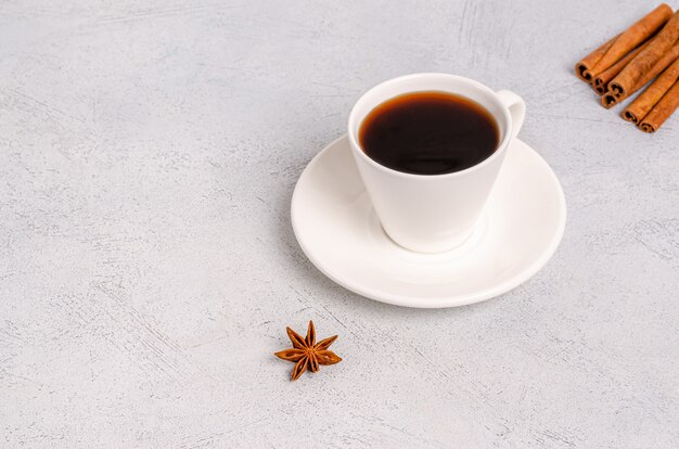 Een kopje zwarte aromatische koffie in een witte kop met anijs sterren en kaneelstokjes op een zachtere achtergrond