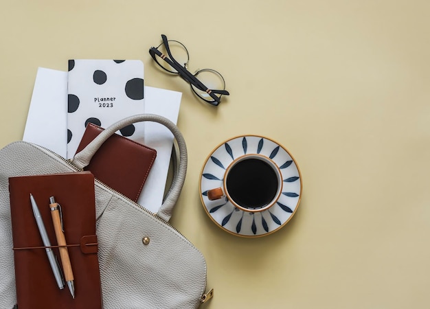 Een kopje zwarte koffie een damestas met accessoires voor kantooronderwijs op een gele achtergrond bovenaanzicht
