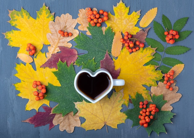 Een kopje zwarte koffie en herfstbladeren op een blauwe houten achtergrond. Hartvormige kop zwarte hete koffie. Liefde voor koffieconcept. Herfstdecor, herfststemming, herfststilleven.