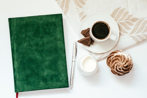 Een kopje zwarte koffie met chocolade en cupcakes en een groen Kladblok