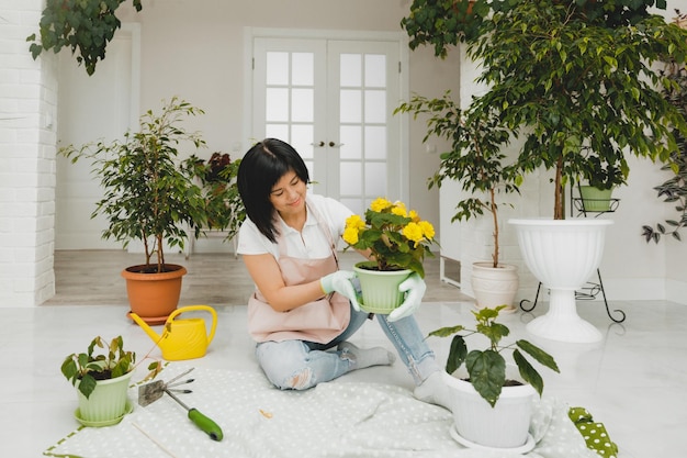 Een Koreaanse vrouw in een schort verzorgt planten en bloemen in een pot Tuinieren en bloementeelt