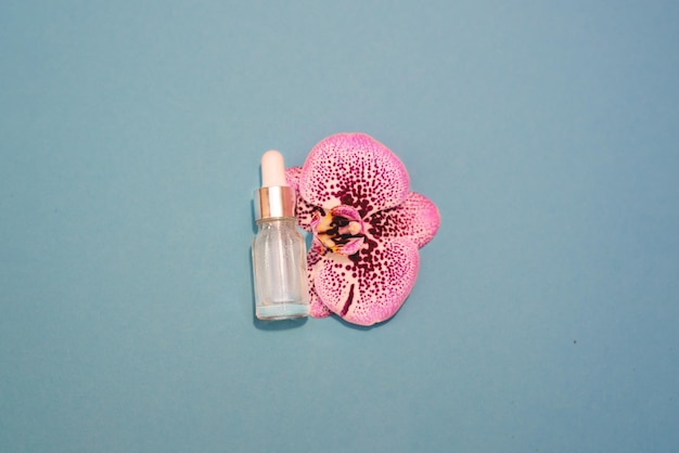 Een kosmetische fles en een roze orchidee op de blauwe achtergrond