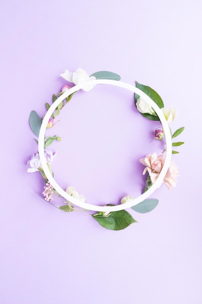 Foto een krans in een rond frame met rozenknoppen, delicate witte bloemen, takken, bladeren en bloemblaadjes op een paarse achtergrond. platte lay-out, bovenaanzicht