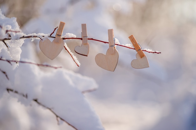 Een krans van houten harten hangt aan een met sneeuw bedekte tak