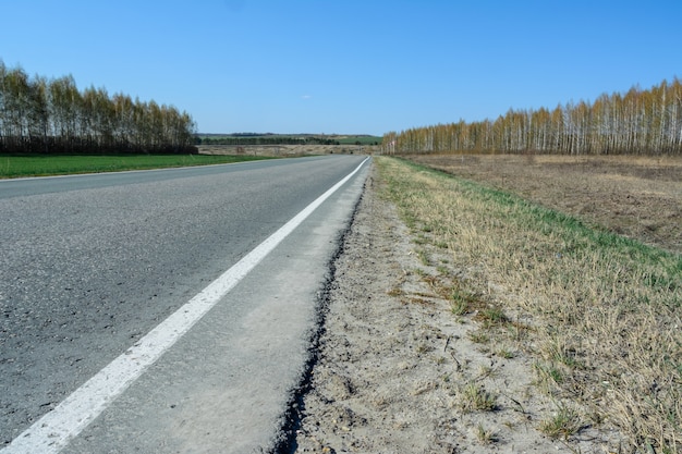 Een kronkelende snelweg die zich uitstrekt tot in de verte tegen de achtergrond van een prachtig lentelandschap, velden, weiden, bossen en heuvels. Wegstrepen op asfalt. Het vooruitzicht om op roadtrip te gaan.