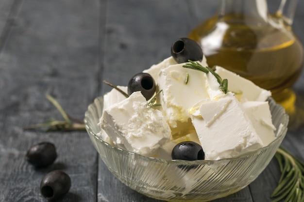 Een kruik olijfolie en een kom fetakaas en olijven op een houten tafel. Natuurlijke kaas gemaakt van schapenmelk.