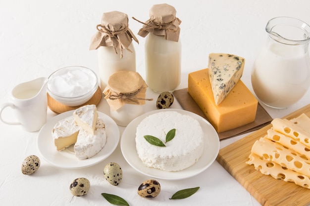 Een kruik verse melk twee flessen kefir en melk kwark zure room en verschillende soorten kaas op een witte achtergrond boerderijproducten