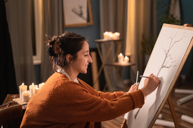 Een kunststudente zit 's avonds in haar huiskamer en tekent een schets van een boomnatuur