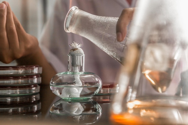 Een laboratoriummedewerker giet vloeistof in een bakje met een laboratoriumjas op tafel.