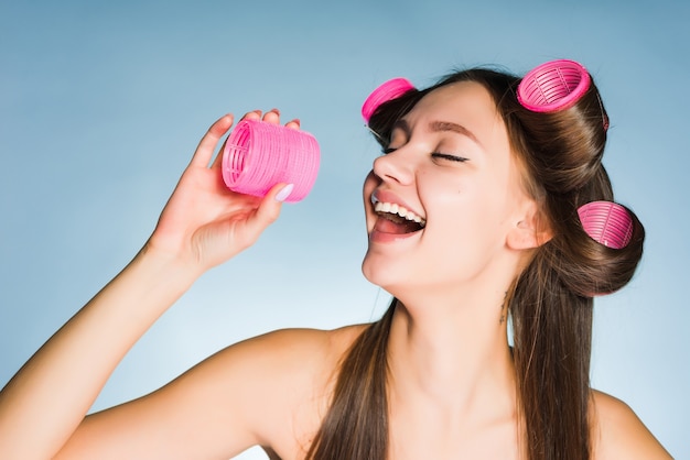 Een lachend jong meisje maakt een modieus kapsel met een grote roze krultang