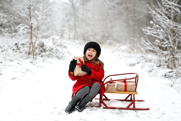 Een lachend meisje zit op een slee in een winterbos op een koude besneeuwde dag