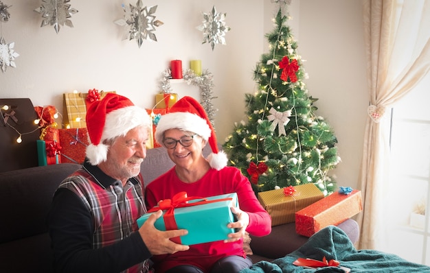 Een lachend paar man en vrouw in Santa's hoeden met veel cadeautjes voor hen en voor familie. Kerstboom op de achtergrond