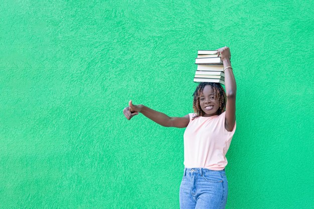 Een lachende Afro-Amerikaanse vrouw houdt een stapel boeken op een groene achtergrond Kopieer de ruimte Onderwijs