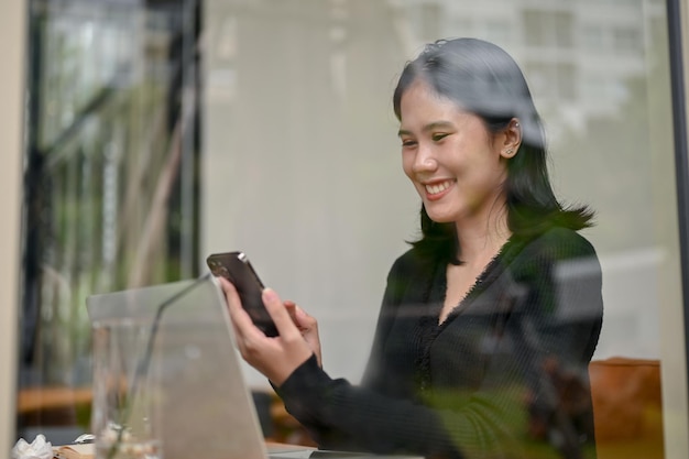 Een lachende Aziatische vrouw kijkt met een blij gezicht naar haar smartphonescherm