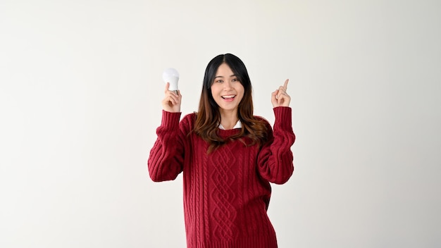 Een lachende Aziatische vrouw wijst haar vinger omhoog en houdt een creatieve idee-inspiratie voor een gloeilamp vast
