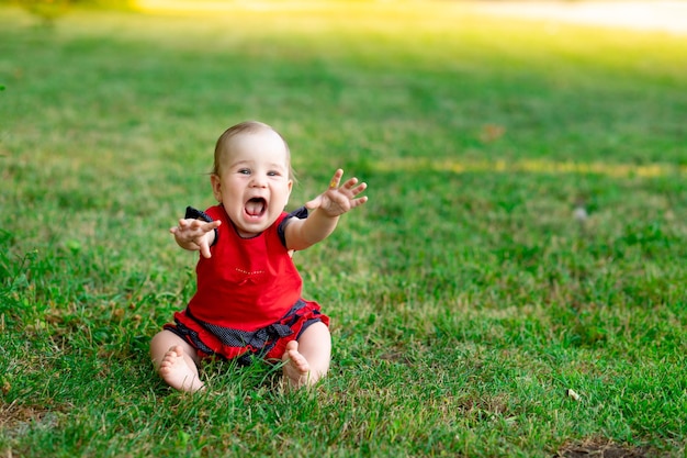 Een lachende baby in de zomer op het groene gras in een rode bodysuit in de ondergaande zon verheugt zich over ruimte voor tekst