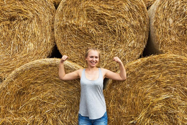 Een lachende jonge vrouw met blond haar staat op de achtergrond van het hooien