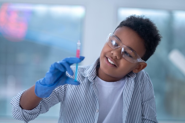 Een lachende jongen met een beschermende bril die een spuit in de hand houdt