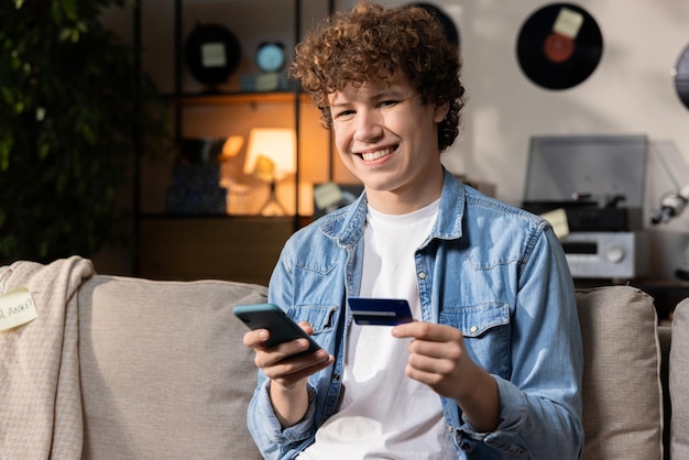 Een lachende jongen zit op een bank en heeft online een overstap gemaakt voor een nieuwe cursus Engels