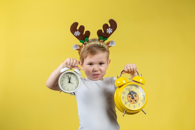 Een lachende kleine jongen in kerstrendierkostuum met twee wekkers