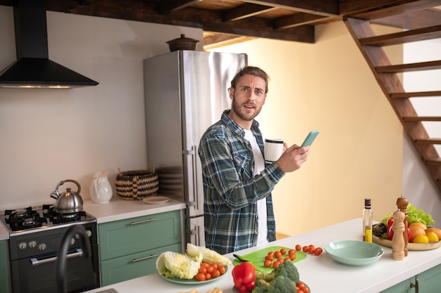 Een lachende man sms't met zijn vriend tijdens het koken