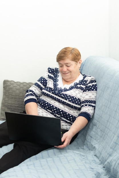 Een lachende oudere vrouw thuis is bezig met e-learning zittend op de bank met een laptop