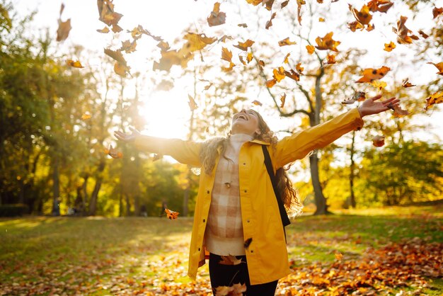 Een lachende toerist in een lichte jas loopt door een herfstpark bij zonnig weer Reisconcept