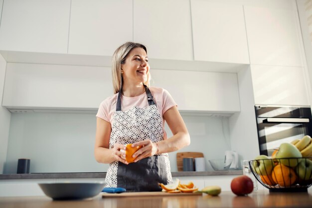 Een lachende vrouw in de keuken die sinaasappel schilt en fruitsalade bereidt