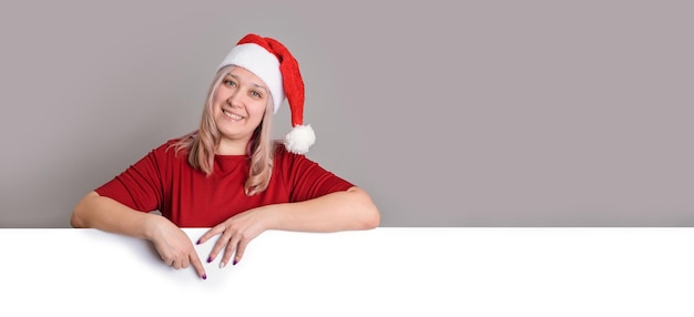 Een lachende vrouw met een kerstmuts wijst naar een leeg leeg bord, een copyspace-banner