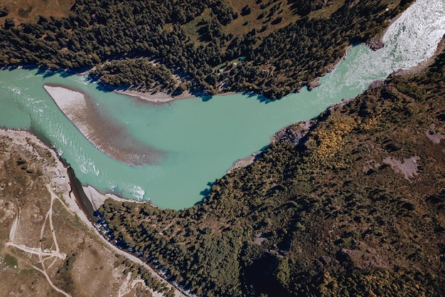 Een landschap gefotografeerd vanuit een helikopter met uitzicht op een sfeervol bos met een stromende heldere turquoise rivier.