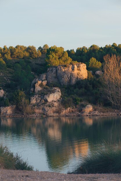 Een landschap met bomen, rotsen en een lagune bij zonsondergang