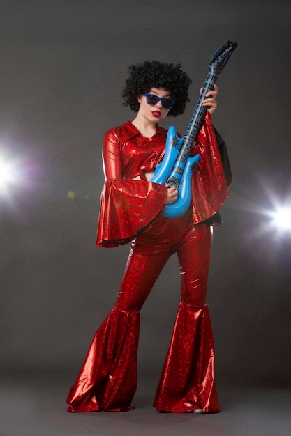 Foto een lang meisje in een flared discostyle podium kostuum houdt een komische gitaar in haar handen