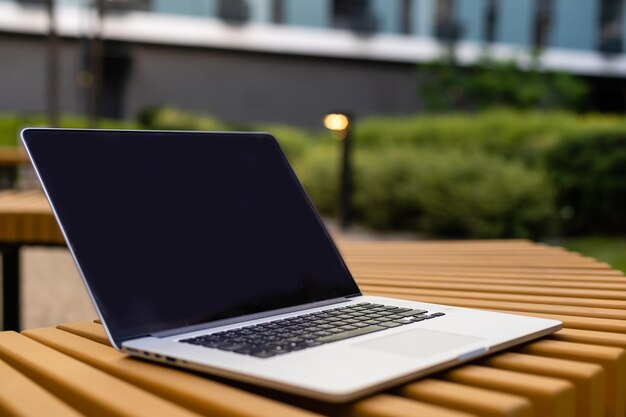 Een laptop met leeg scherm staat op een houten bankje op de binnenplaats, werkruimte van freelancer in prachtige huistuin