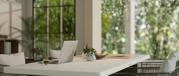 Een laptop op een eettafel in een moderne eetkamer met een prachtig groen uitzicht op de natuur