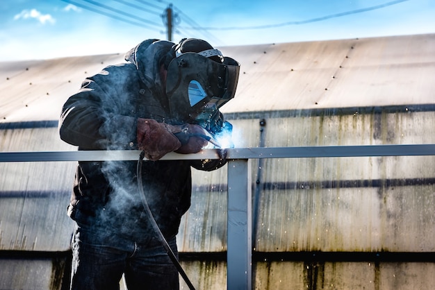 Een lasser die een veiligheidshelm en handschoenen draagt, last een metalen hek