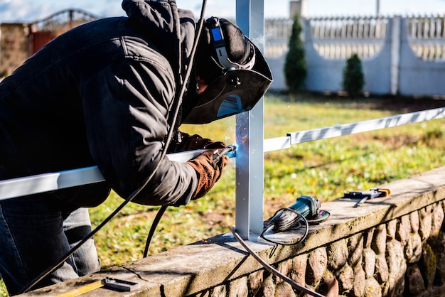 Een lasser die een veiligheidshelm en handschoenen draagt, last een metalen hek