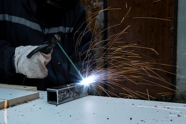 Een lasser met constructiehandschoenen en een lasmasker is buiten gelast met een lasmachine metaal